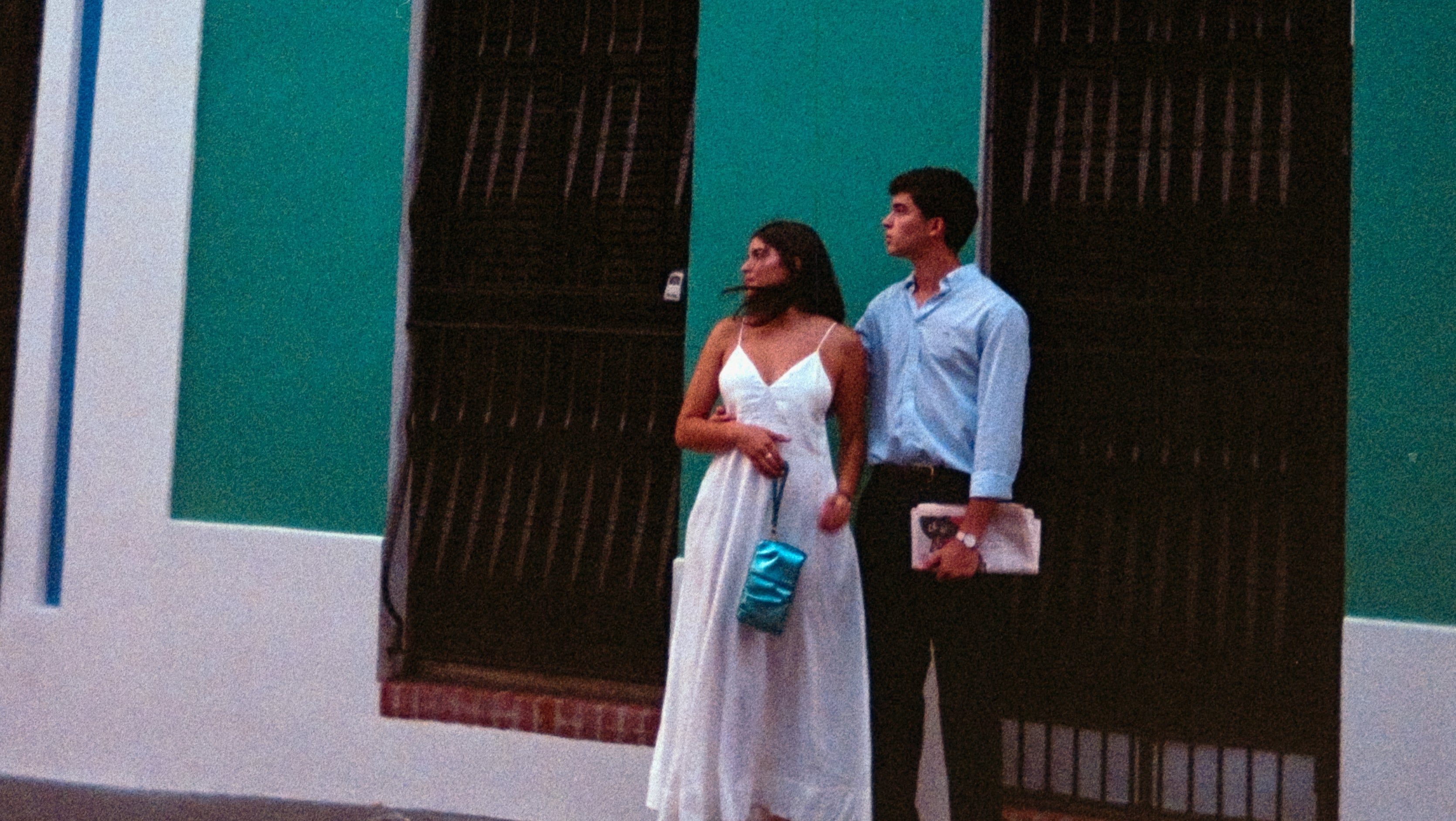 Couple standing in front of a colorful building with a teal wall and white accents.