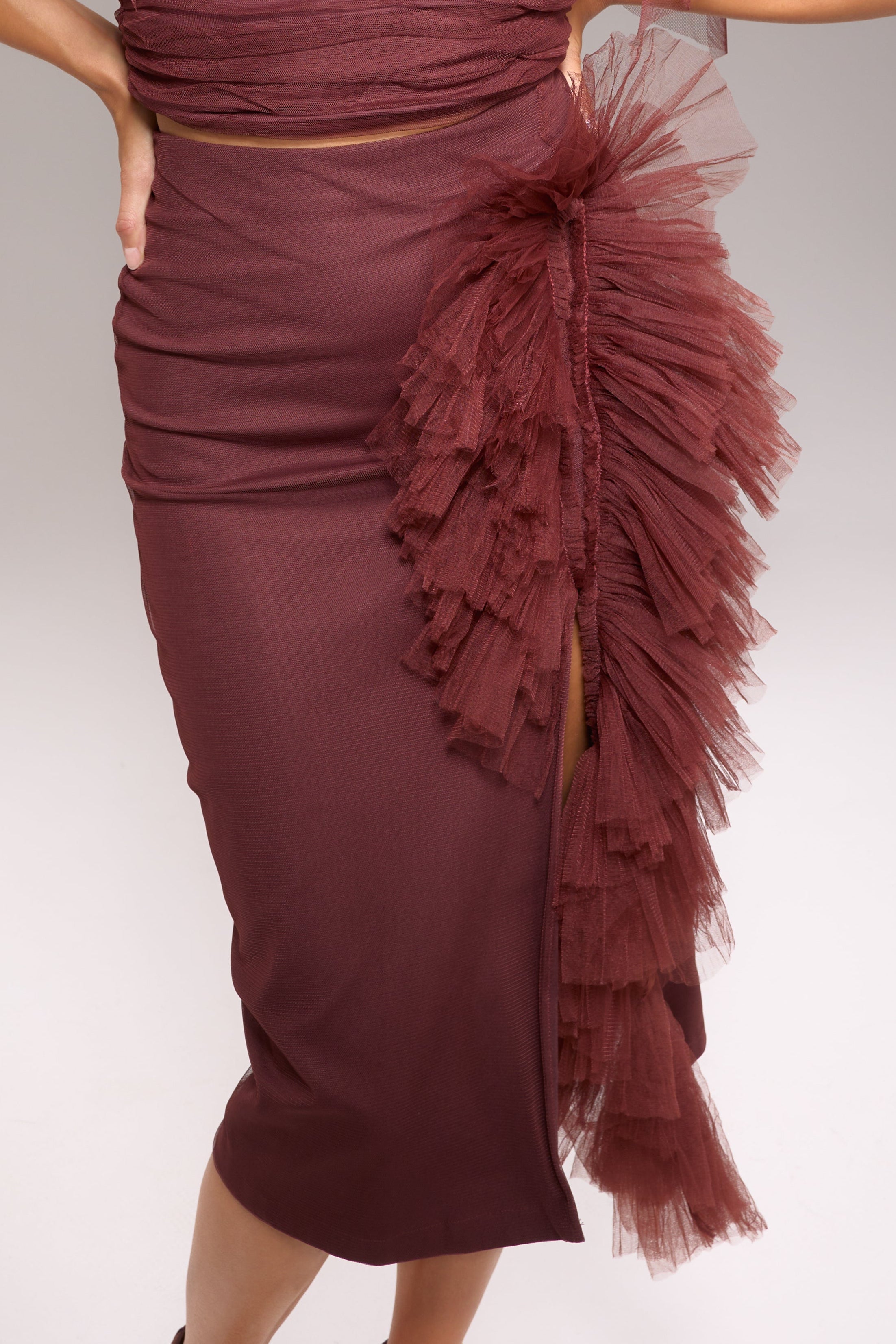 A model wearing a maroon skirt with tulle details. The skirt is midi length and has a back zipper.