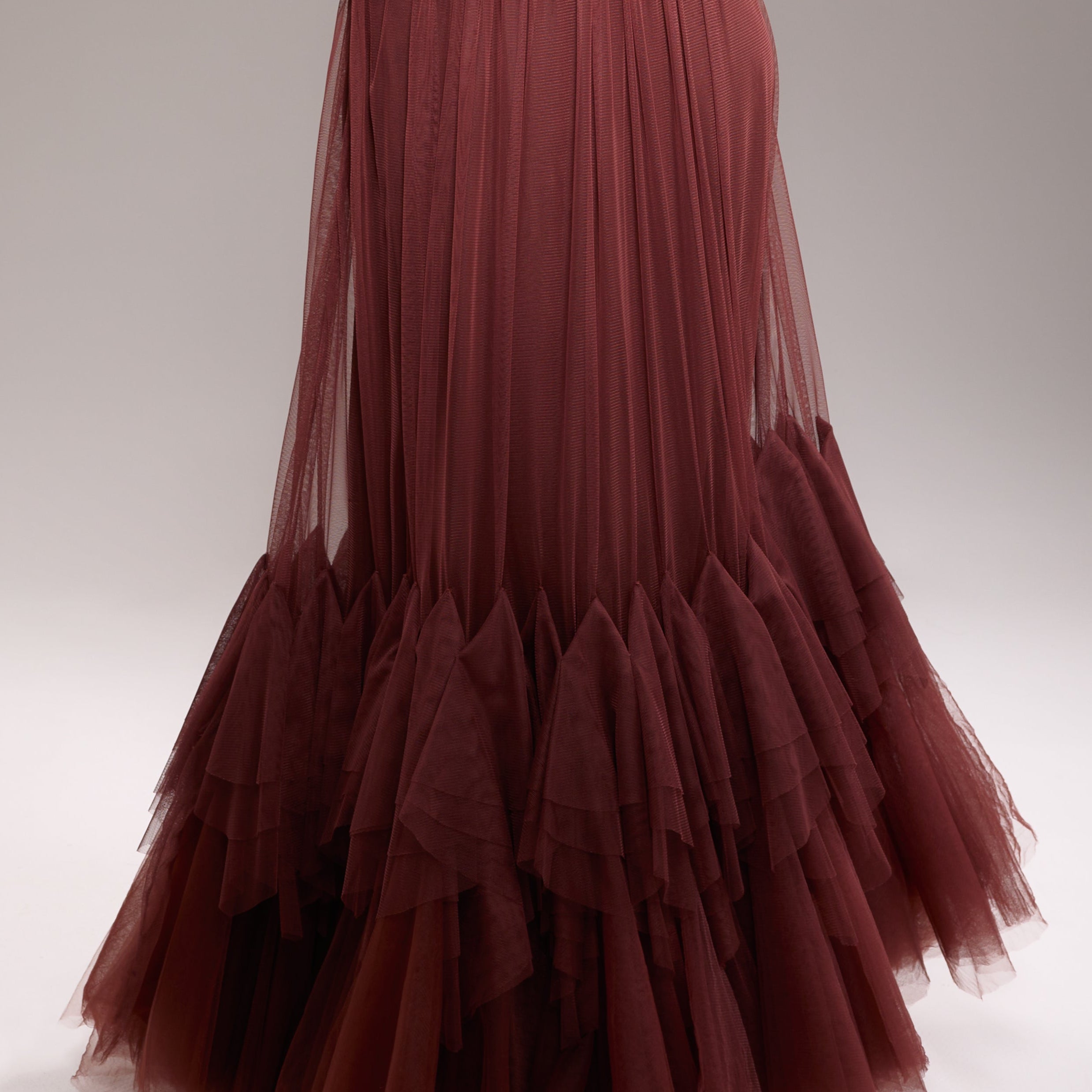 A woman wearing a maroon tulle and mesh strapless dress with a floor-length design, featuring a back zipper.