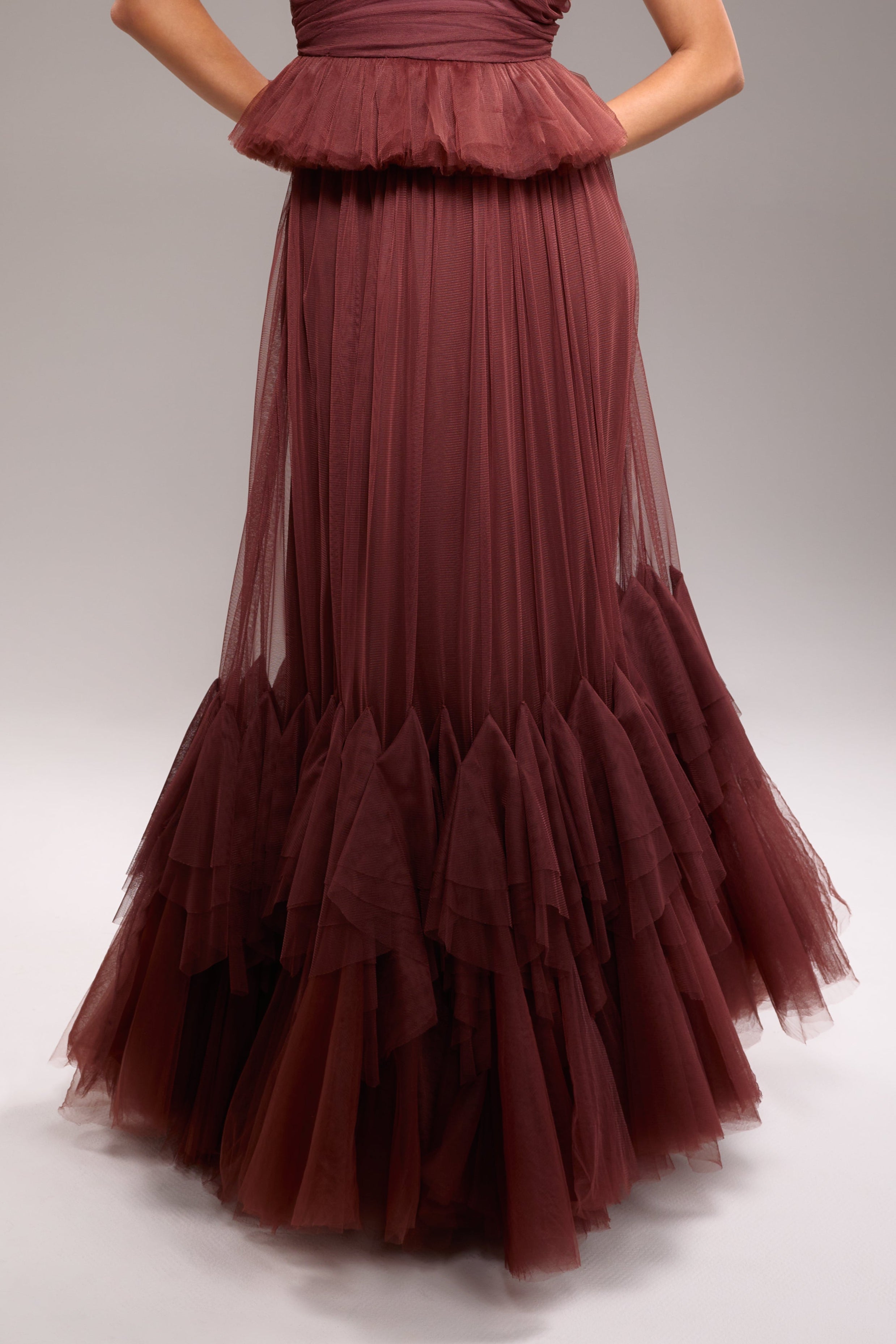 A woman wearing a maroon tulle and mesh strapless dress with a floor-length design, featuring a back zipper.