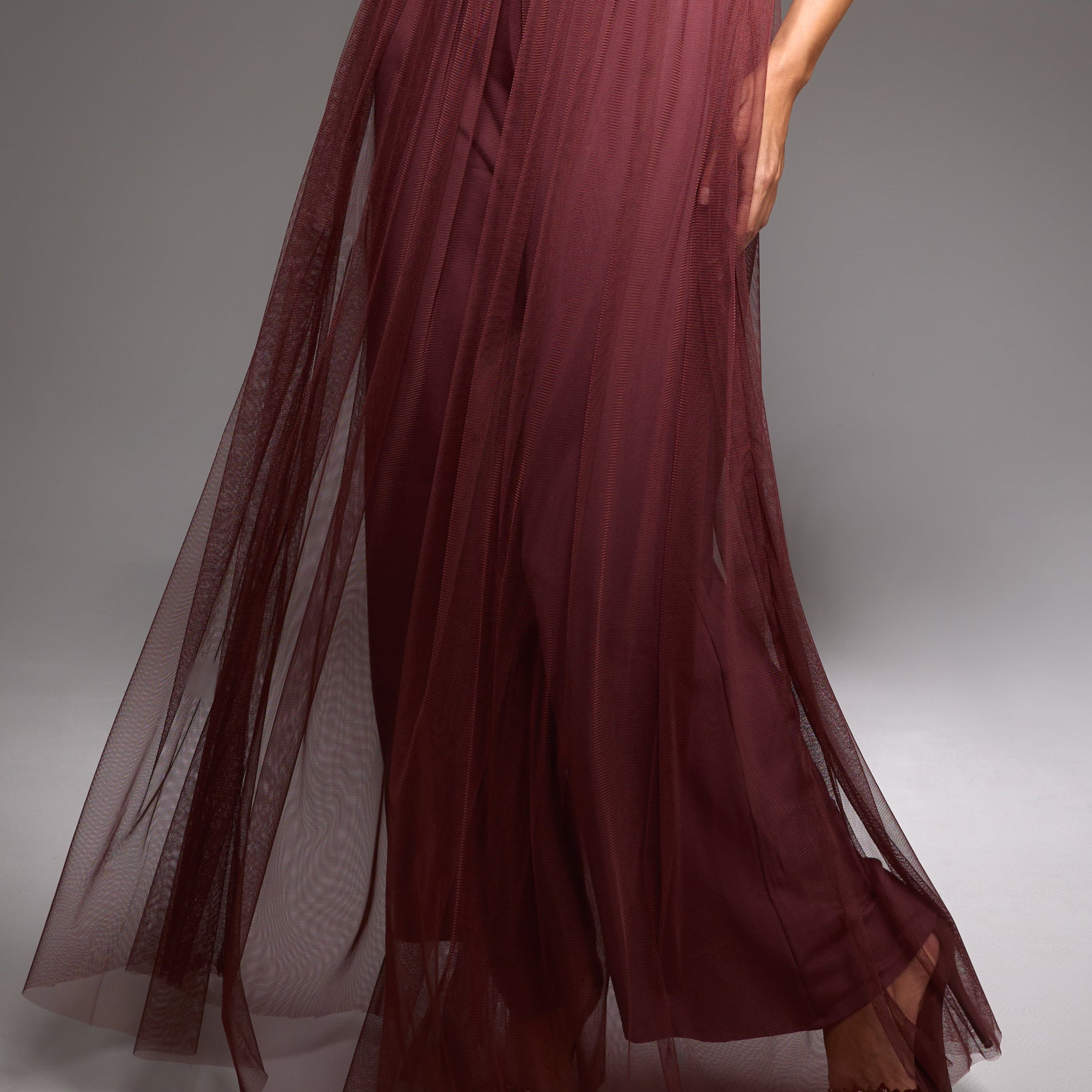 Model wearing a burgundy ruffled top and skirt set against a gray background