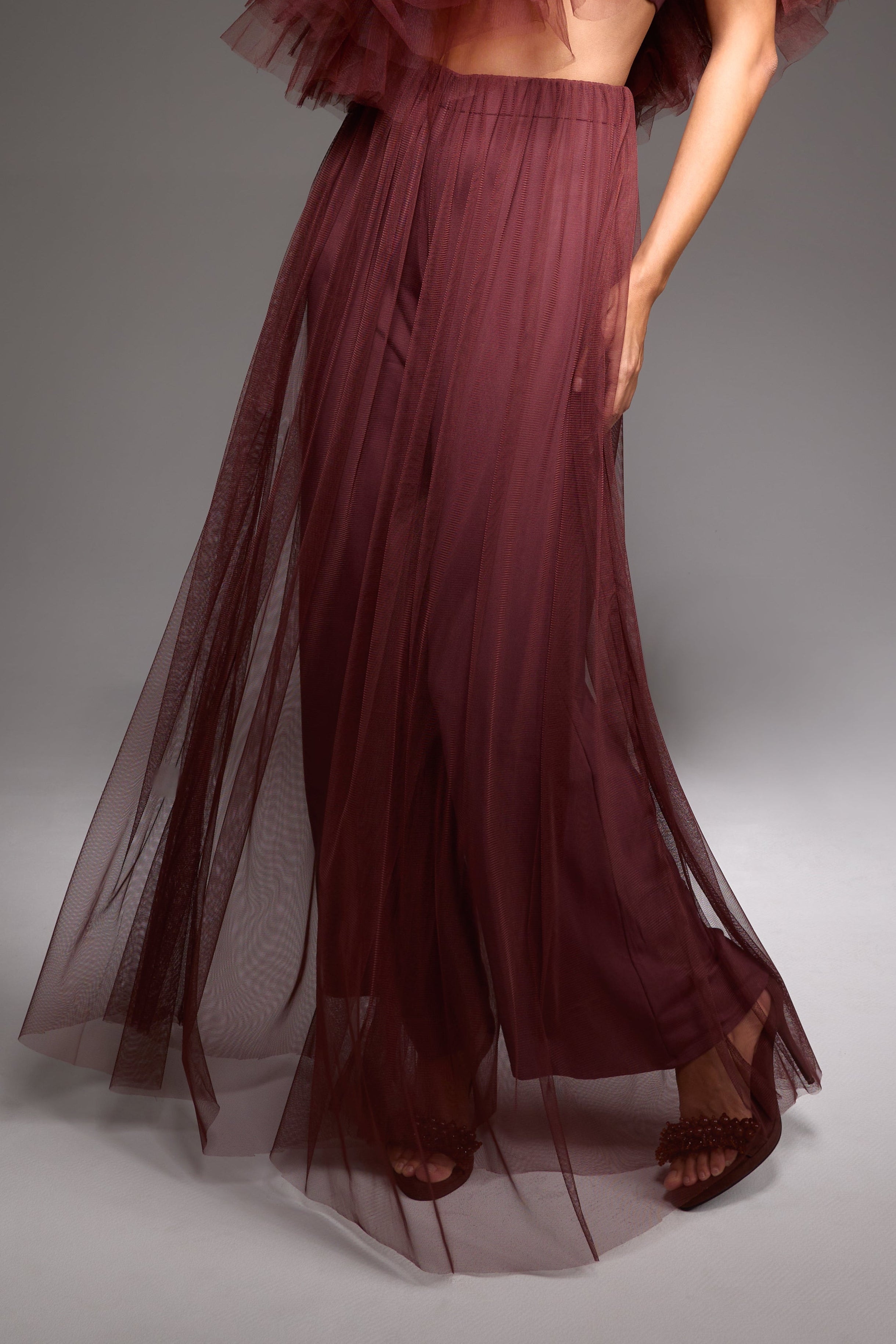 Model wearing a burgundy ruffled top and skirt set against a gray background