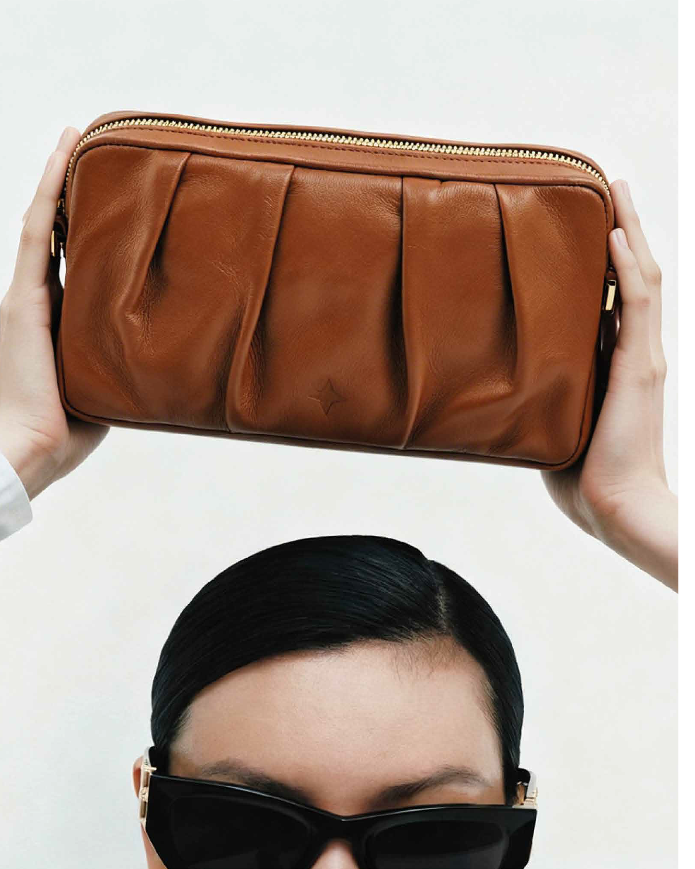 Person holding a brown leather clutch above their head with a plain background